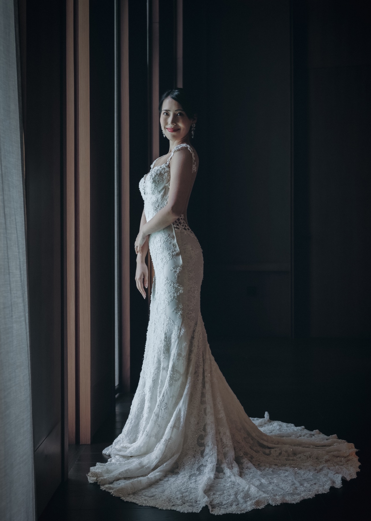 A bride in a lace wedding dress by a softly lit window