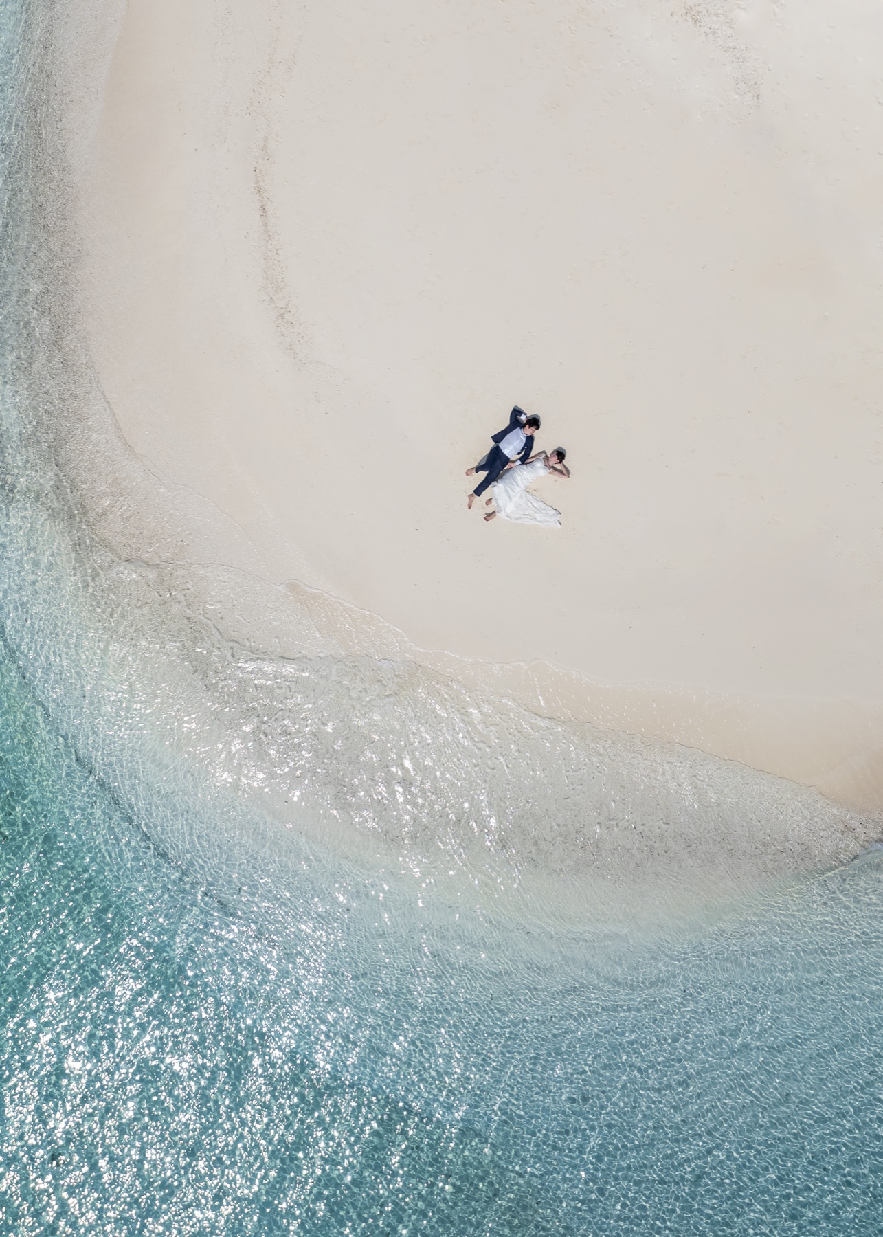 A newlywed couple relaxing on a Maldives sandbank beside clear water