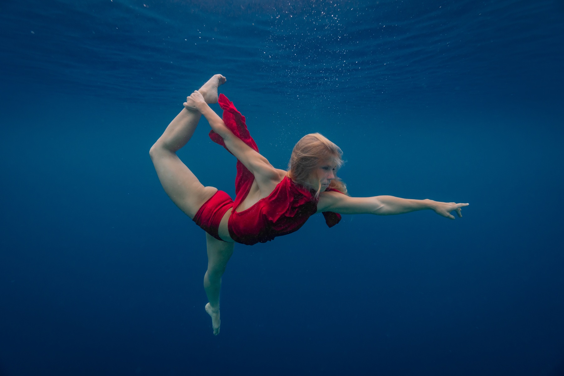 A woman in a red dress moving through deep blue water